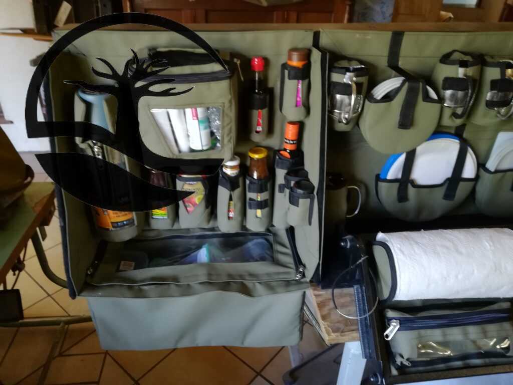 Custom Canvas Caddie to hold dishwashing essentials, a Stanley flask, condiments and spices with a dropdown bag to store grocery items, Melamine plates and bowls, paper plates and holder, Stainless steel mugs and glasses (glas) with a flip-out shelf to hold a removable bag, a zipped bag with a clear PVC window and a papertowel holder fitted to an aluminum Bakkie canopy.