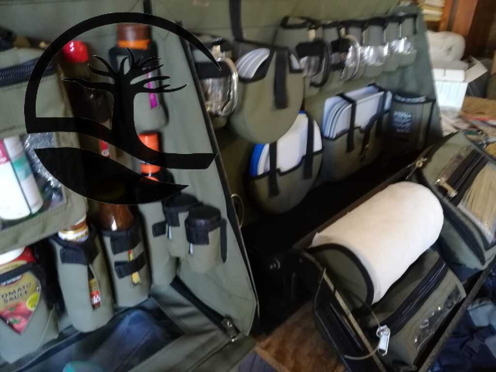 Custom Canvas Caddie to hold dishwashing essentials, a Stanley flask, condiments and spices with a dropdown bag to store grocery items, Melamine plates and bowls, paper plates and holder, Stainless steel mugs and glasses (glas) with a flip-out shelf to hold a removable bag, a zipped bag with a clear PVC window and a papertowel holder fitted to an aluminum Bakkie canopy.
