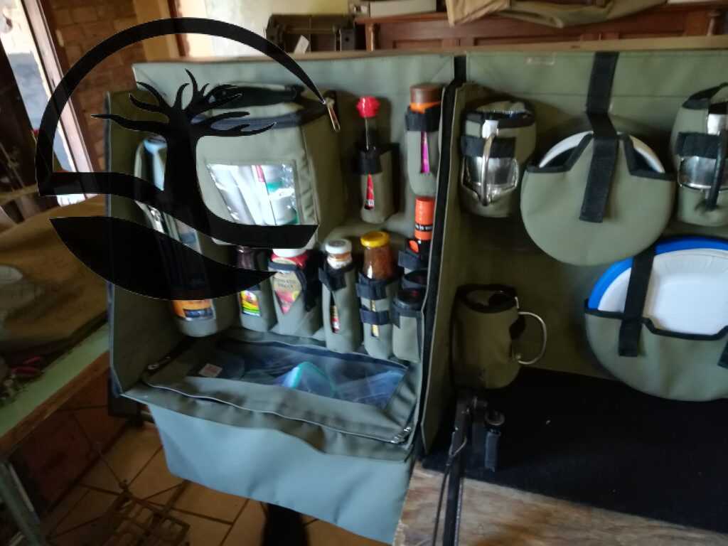 Custom Canvas Caddie to hold dishwashing essentials, a Stanley flask, condiments and spices with a dropdown bag to store grocery items, Melamine and plastic plates and bowls and stainless steel mugs fitted to an aluminum Bakkie canopy.