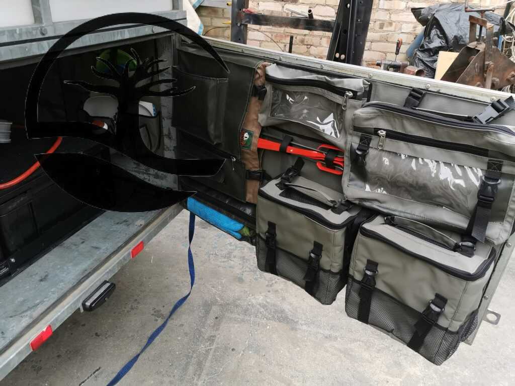 Custom Canvas caddie with removable shower bags and first aid bag, with zipped pockets with clear PVC windows and a braaigrid bag fitted to the back door of a Buzzard camping trailer.