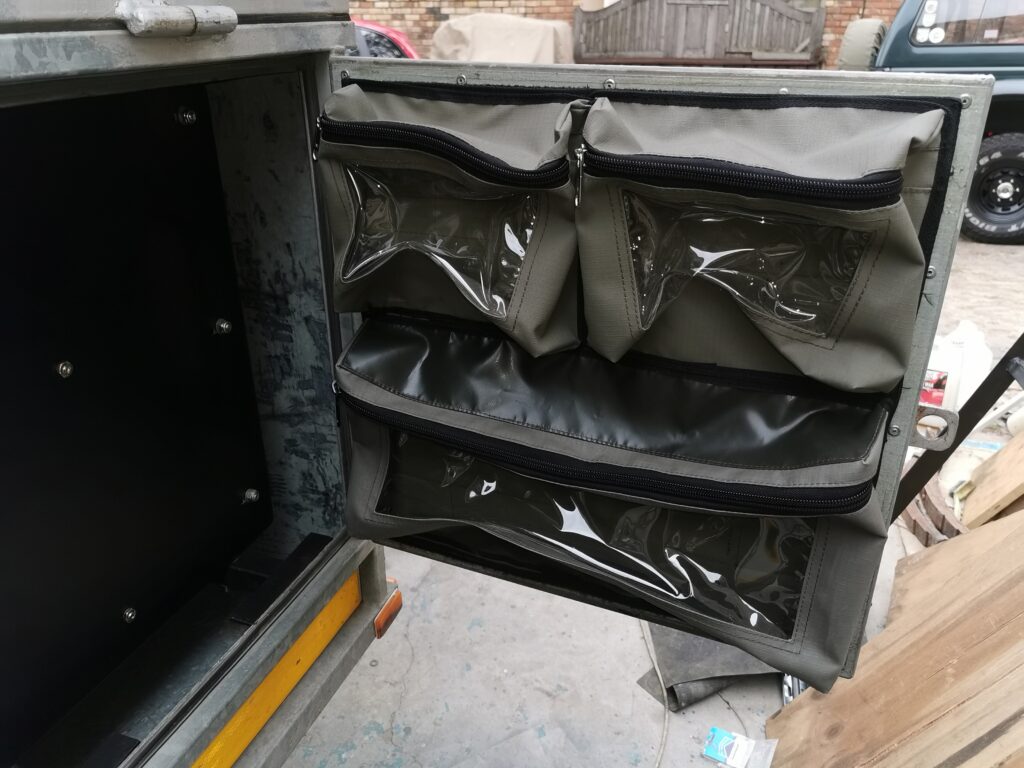 Custom Canvas Caddie with fixed zipped bags fitted in the front door of a Buzzard Camping Trailer.